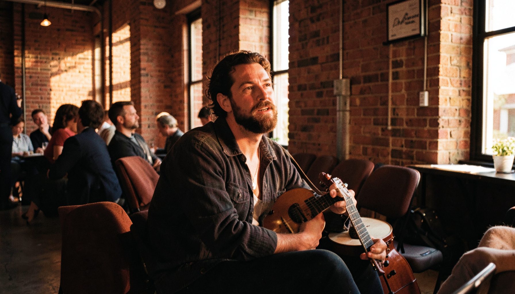 An arts-sector speaker seated with a musical instrument nearby, warm golden-hour light filling a relaxed conference lounge