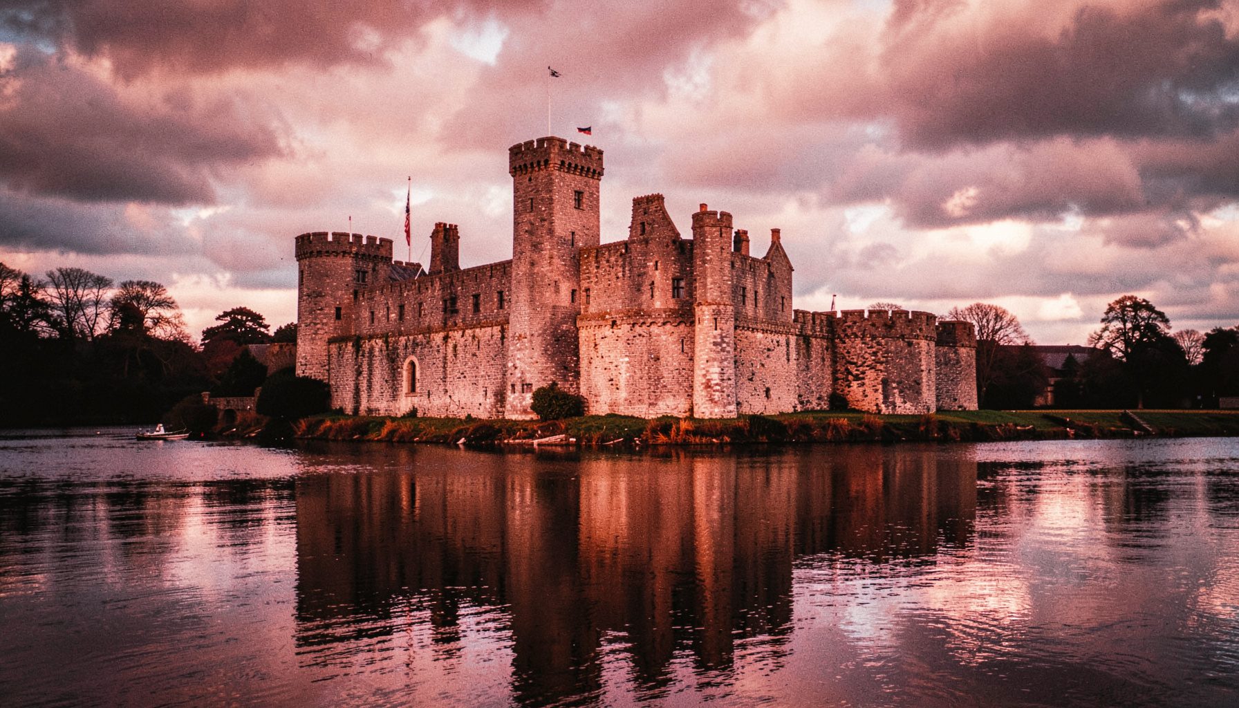 King John's Castle standing on the banks of the River Shannon under a dramatic cloudy sky, stone walls reflected in the water