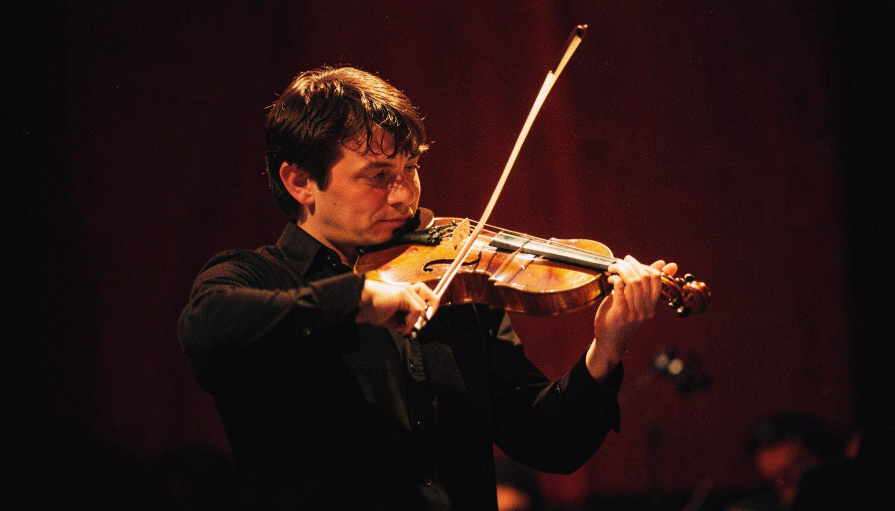 Violinist performing on a dimly lit stage, warm golden spotlight, deep burgundy backdrop